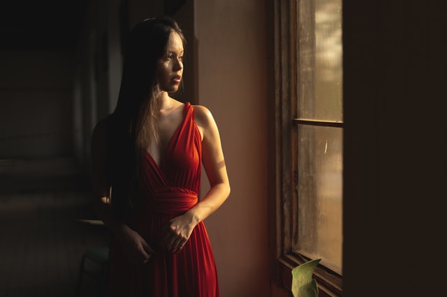 Dívka v červených společenských šatech stojící u okna